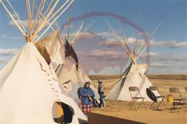 Two people standing by tipis and stage