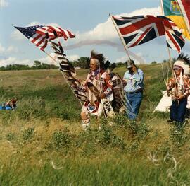 Henry Beaudry in traditional regalia bearing a sacred eagle staff while leading the ceremonial pr...