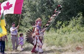 Henry Beaudry in traditional regalia bearing a sacred eagle staff while leading the ceremonial pr...