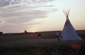 Two people standing by tipi at dusk