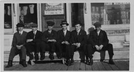 Six men seated on sidewalk