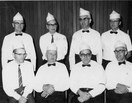 Eight clergymen wearing white shirts, bowties, and chef hats