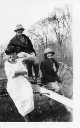 Three unidentified women seated on horse drawn hay rake