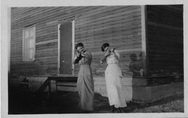Two women wearing long dresses pointing .22 rifles