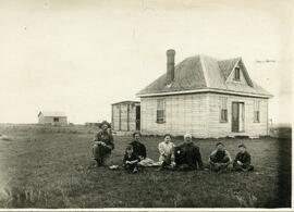 Family on ground in front of house with prairie background